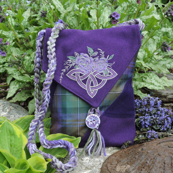 Purple bag with floral embroidery and tartan pattern, surrounded by greenery and flowers.